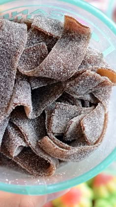 a person holding a glass bowl filled with powdered sugary pastries on top of fruit