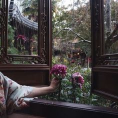 a woman sitting on a window sill with flowers in her hand and looking out the window