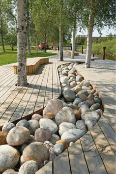 there are many rocks and benches on the wooden flooring in this park area that is lined with trees