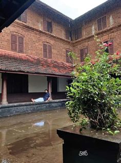 a man laying on the ground in front of a building next to a tree and water