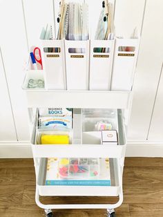 a white cart filled with lots of craft supplies on top of a hard wood floor