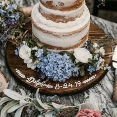 a wedding cake with white frosting and blue flowers sits on a wooden platter