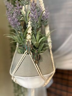 a potted plant hanging from a rope with purple flowers in it and greenery