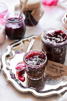 two jars of jam sit on a silver platter next to spoons and forks