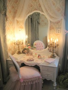 a white desk with a mirror, chair and lights on it in a room that has pink wallpaper