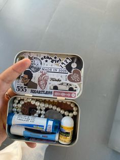 a person holding an open tin with various items in it and some writing on the inside