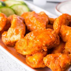 some chicken wings are on a plate with cucumbers and dipping sauce in the background