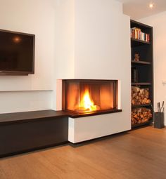 a fire place in a living room with wood stacked on the floor and a flat screen tv mounted above it