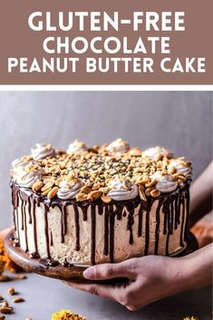 a person holding a cake with chocolate frosting and nuts on top, in front of flowers