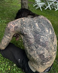 a man sitting in the grass with his back to the camera, covered in tattoos