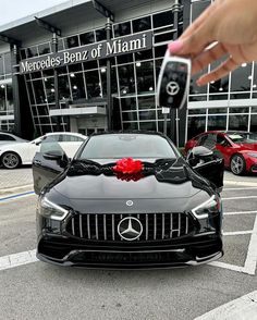 a person holding a car key in front of a black mercedes benz of miami dealership