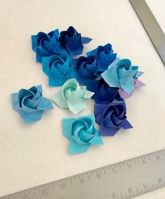 blue and green origami flowers sitting on top of a white table next to a ruler