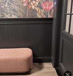 a bench in front of a wall with flowers on it and the door to another room