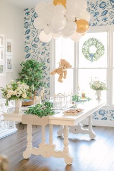 a blue and white baby shower with balloons hanging from the ceiling, teddy bear on the table