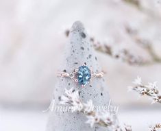 a blue ring sitting on top of a rock next to snow covered plants and branches