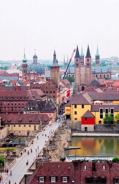 an aerial view of a city with buildings and water in the foreground, surrounded by tall spires