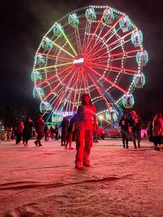 a ferris wheel lit up at night with people walking around in the foreground and onlookers