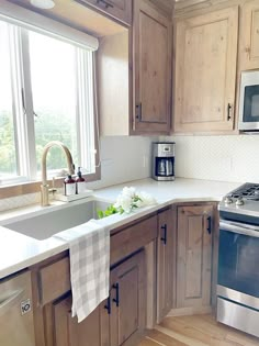 a kitchen with wooden cabinets and stainless steel appliances, including a dishwasher, stove, sink, microwave and window