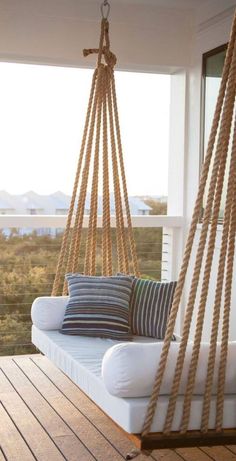 a white couch sitting on top of a wooden floor next to a swing chair with pillows