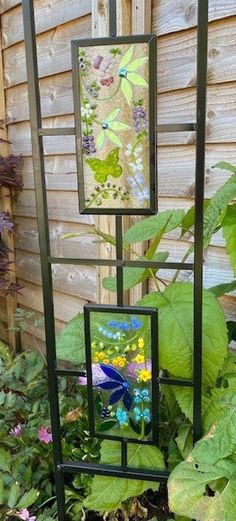 three stained glass panels sitting on top of a metal stand in front of some plants