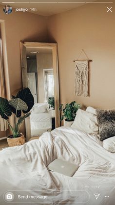 a bed with white sheets and pillows next to a mirror in a room filled with plants