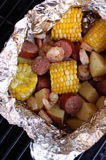 corn on the cob with sausage and potatoes in foil wrapped over an open grill