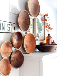 several wooden bowls are hanging on the wall above a white cabinet with a metal sign