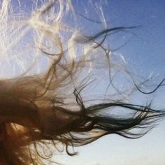 a woman with her hair blowing in the wind on a sunny day at the beach