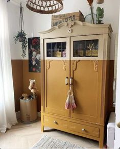 an old fashioned cabinet is painted yellow and has some decorations hanging from the ceiling above it