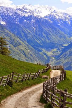 a dirt road going up the side of a hill with snow capped mountains in the background