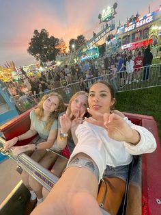 three girls are riding on a roller coaster at an amusement park with their hands in the air