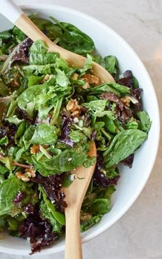 a salad in a white bowl with wooden spoons