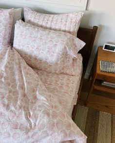 a bed with pink sheets and pillows on top of it next to a night stand