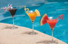 three cocktails sitting on the edge of a swimming pool