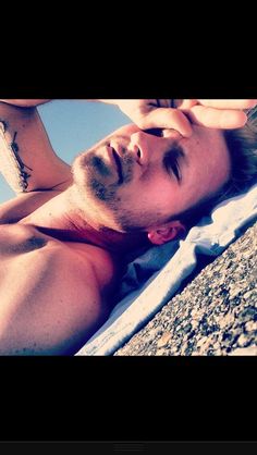 a man laying on top of a beach next to the ocean with his eyes closed