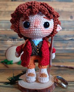 a crocheted doll is standing on top of a piece of wood and holding a stick