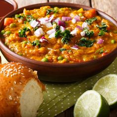 a bowl of soup with bread and limes on the side, next to it