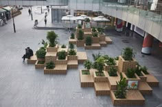 people are walking around in an open area with wooden benches and planters on the floor