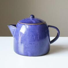 a blue ceramic teapot with a gold rim on a white countertop, in front of a gray wall