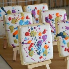 decorated cookies sitting on top of wooden easels with paint splattered on them