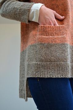 a woman's hand is in the pocket of her orange and grey striped sweater