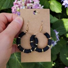 a person holding up a pair of black beaded hoop earrings in front of some flowers