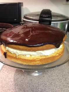 a chocolate covered dessert sitting on top of a glass cake plate next to an oven