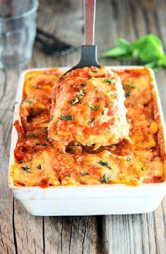 a casserole dish with meat and cheese in it on a wooden table next to a glass of water