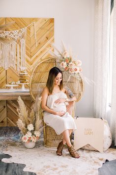 a pregnant woman sitting in a wicker chair with her baby on her lap and holding a bird