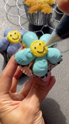 a hand holding a small cupcake with blue frosting and yellow smiley faces on it