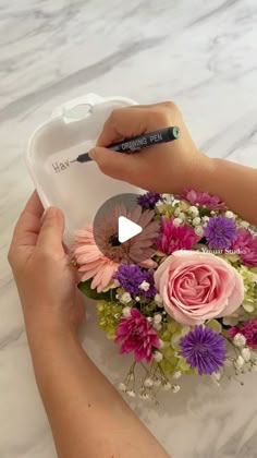 a person is holding a flower arrangement with a marker in their hand and writing on it