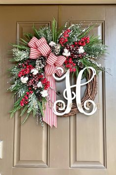 a christmas wreath with the letter h hanging on a front door decorated with holly, berries and pine cones