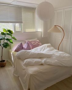 a white bed sitting under a window next to a potted plant and wooden floor