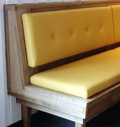 a wooden bench with yellow leather upholstered seat and back rest, in front of a white wall